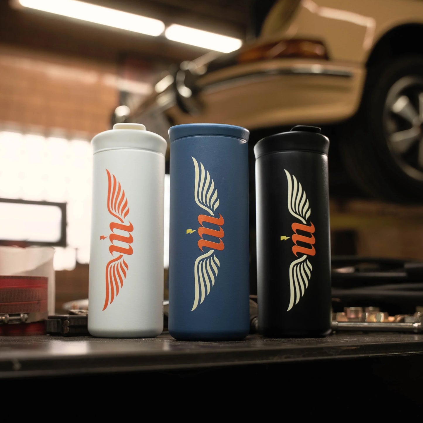 Three tumblers with a logo on a workbench in a garage setting