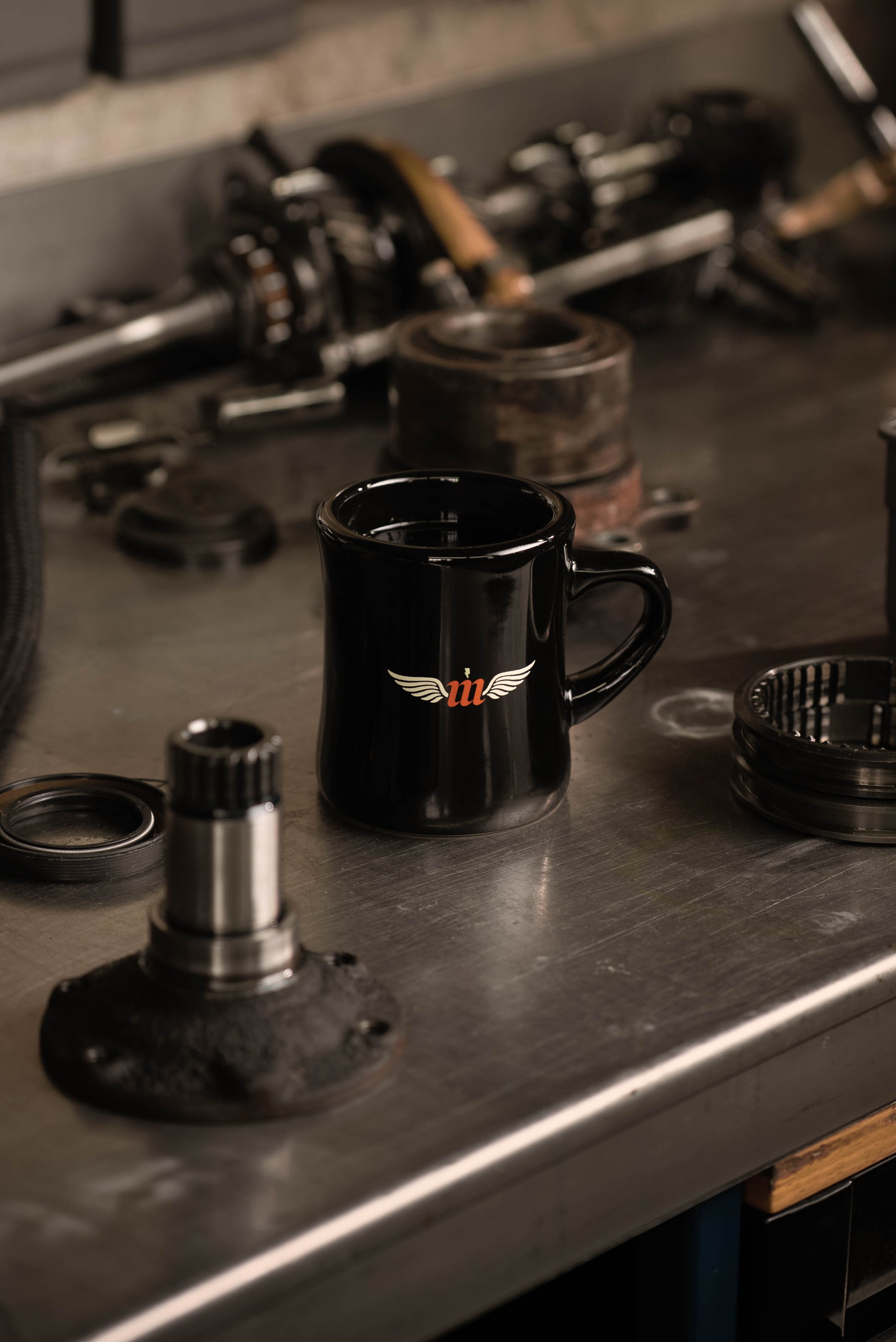 Black mug with a logo on a metal surface with mechanical parts