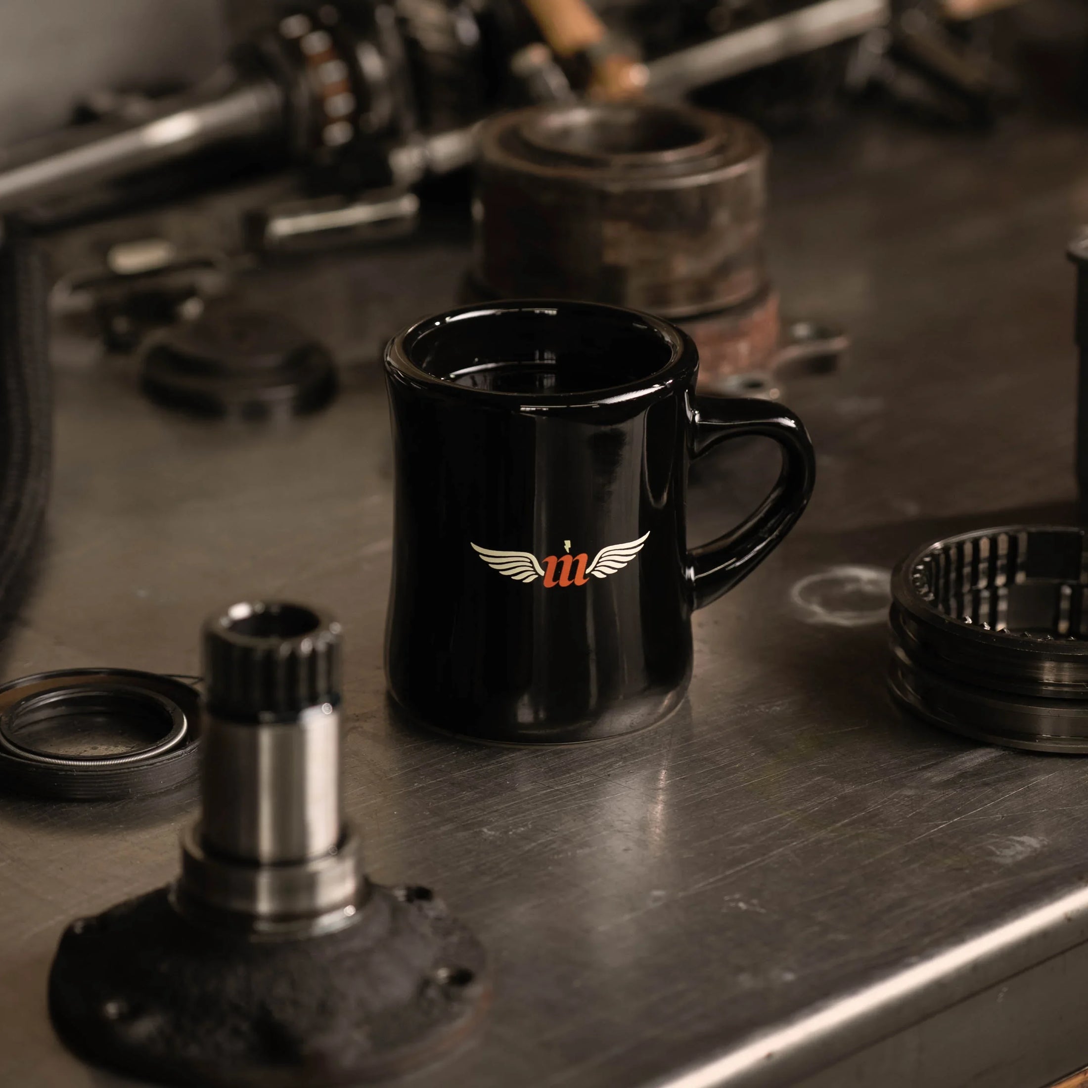 Black mug with a logo on a metal surface with mechanical parts