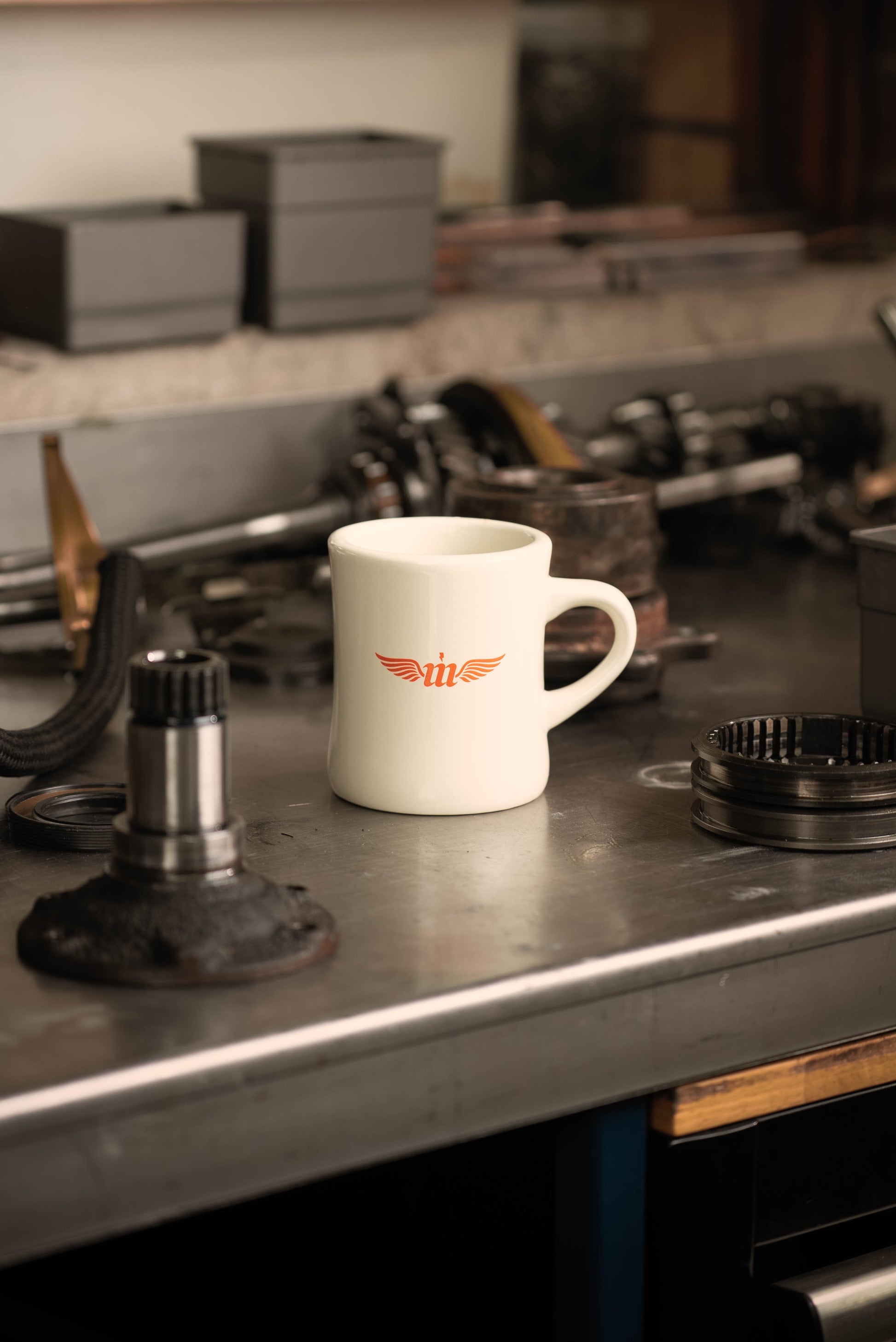 White mug with a logo on a metal workbench with mechanical parts