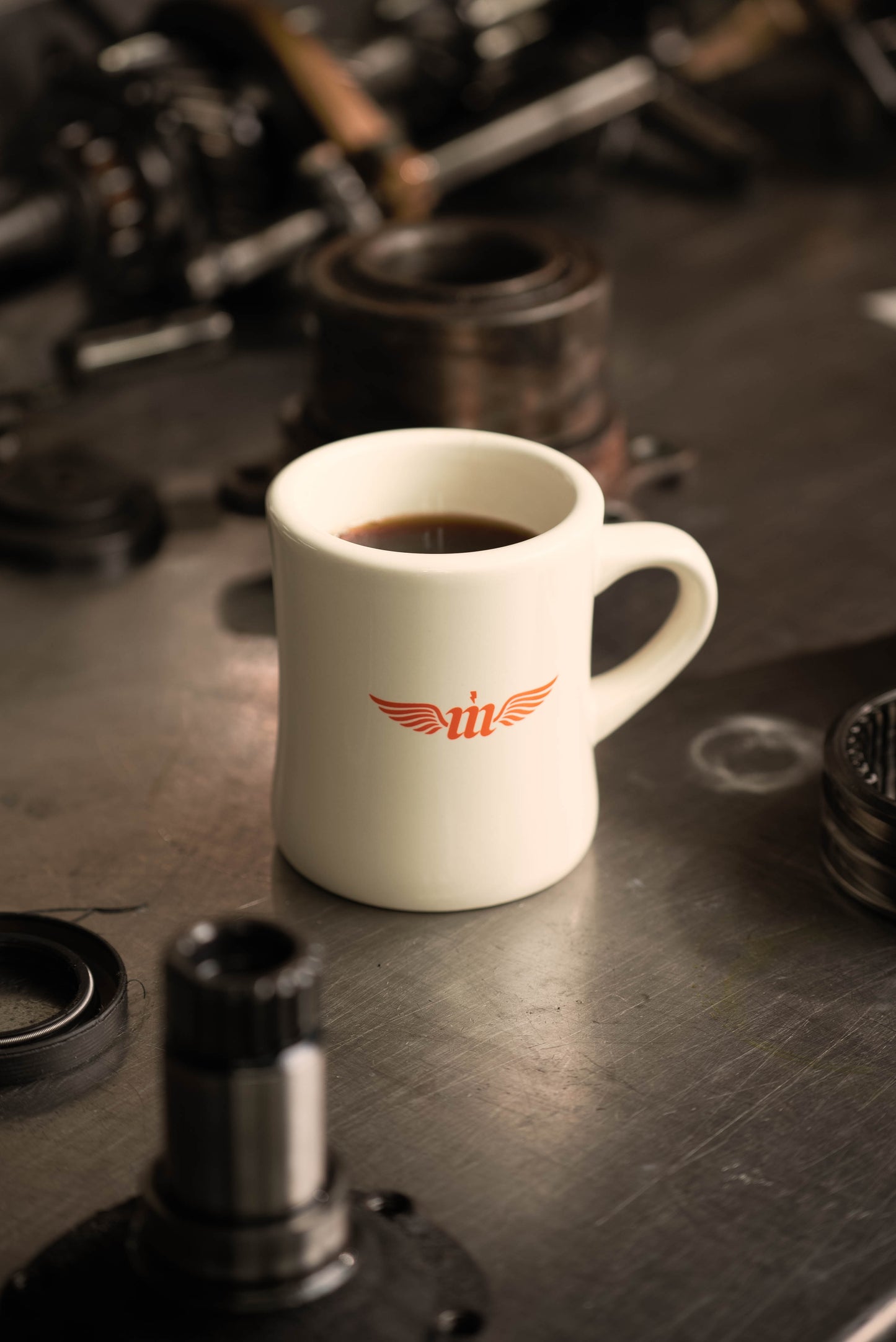 coffee filled cream colored  Motovator logo Vintage Diner mug on a metal workbench with car parts