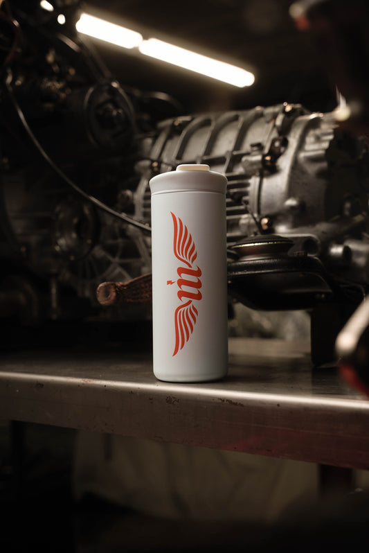 White and red Motovator travel mug on a workbench by a transmission