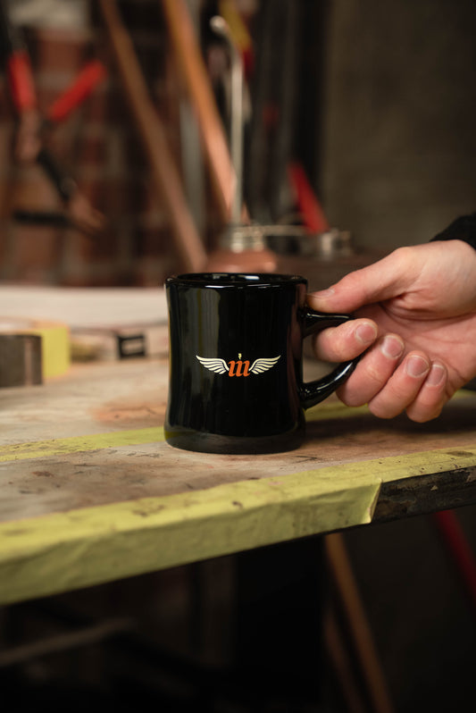 Black Motovator logo Vintage Diner mug on a workbench with hand