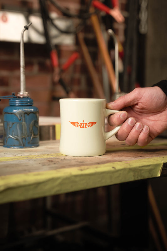 Cream Motovator logo Vintage Diner mug on a workbench with hand